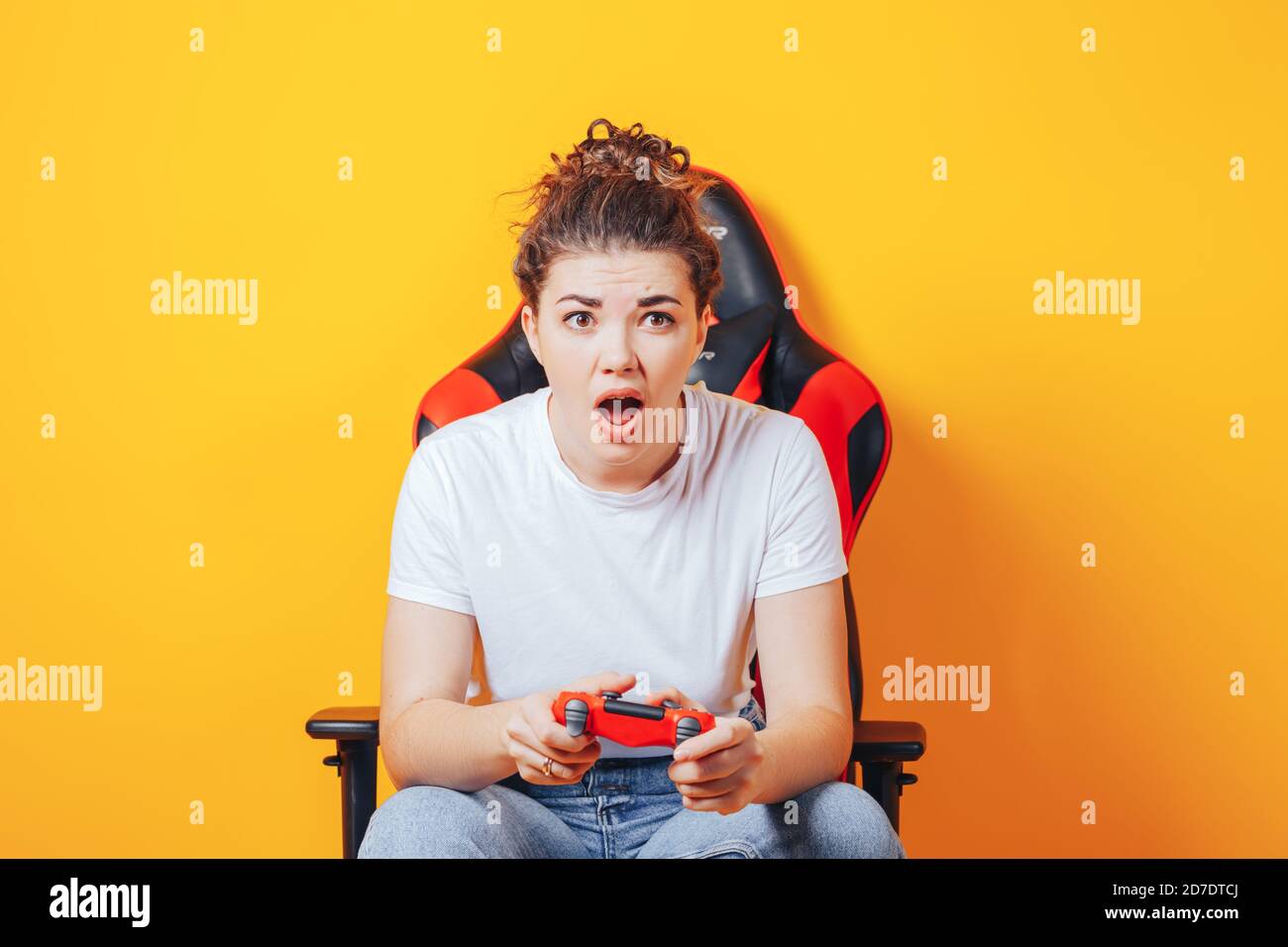 Frau, die hinter einem Spielstuhl in ihren Händen sitzt und rot hält Gamepad auf gelbem Hintergrund Stockfoto