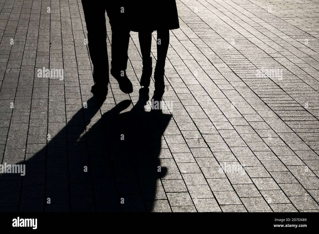 Ein Paar, das die Straße entlang geht, Silhouetten und Schatten von Mann und Frau auf dem Fußgängerweg. Männliche und weibliche Beine, Beziehungskonzept Stockfoto
