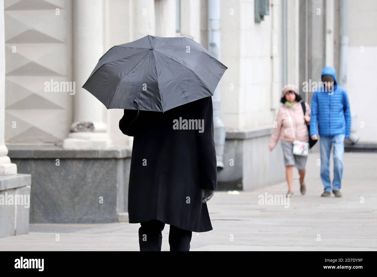 Regen in einer Stadt, Mann im Herbstmantel mit schwarzem Regenschirm, der auf einer Straße läuft. Menschen in regnerischem Wetter, Herbstsaison Stockfoto