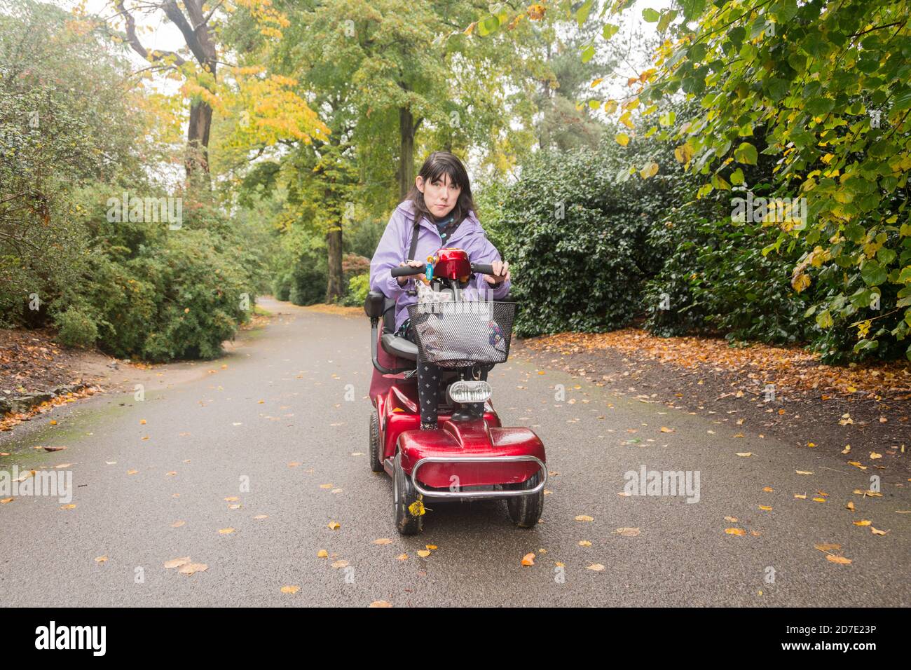 Nahaufnahme einer jungen Frau, die einen Mobilitätsroller umzingelt fährt Durch Pflanzen und Gärten Stockfoto
