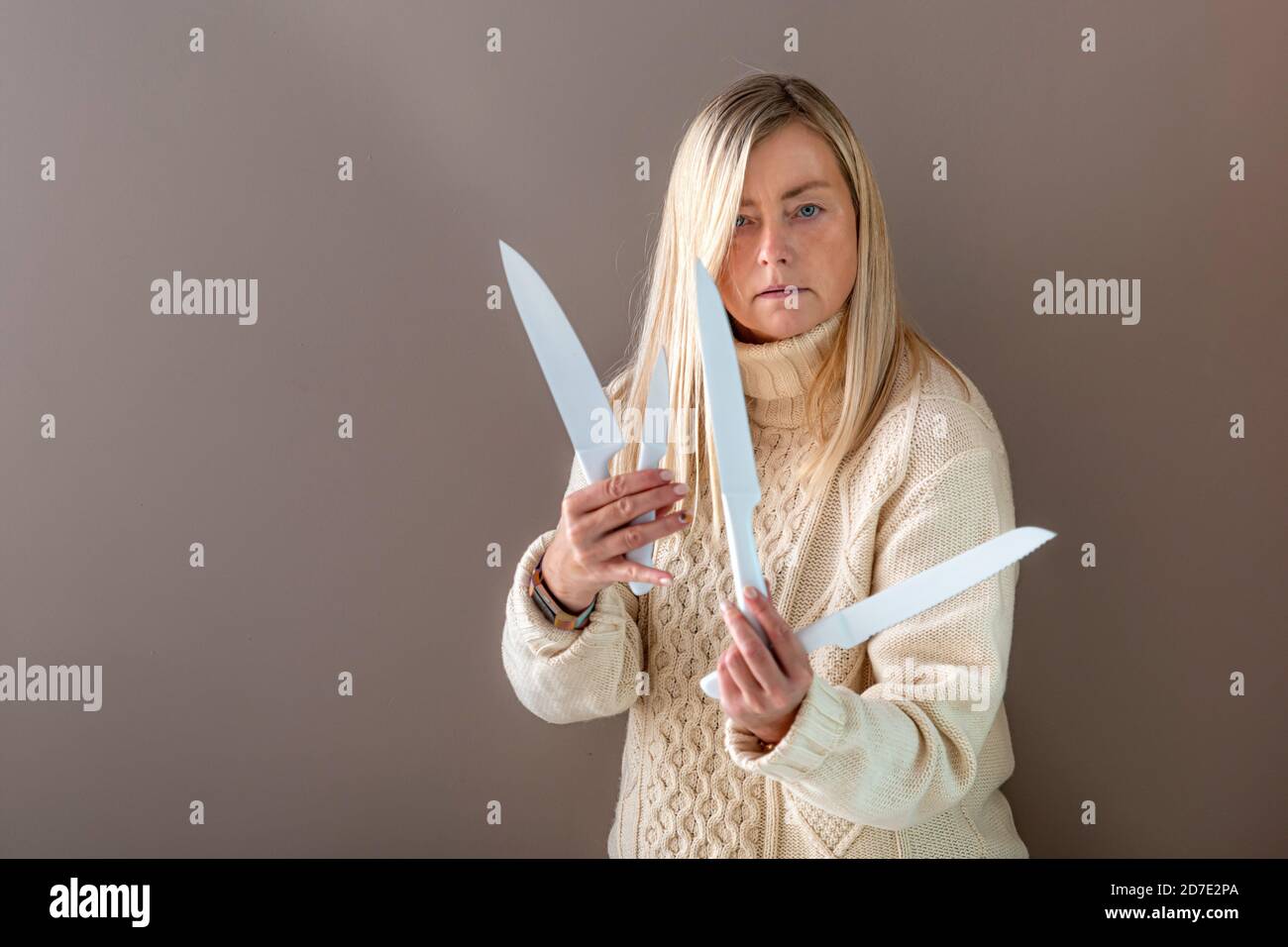 Blonde Frau gestikuliert emotional mit Messern, isoliert auf einem dunklen Hintergrund Stockfoto