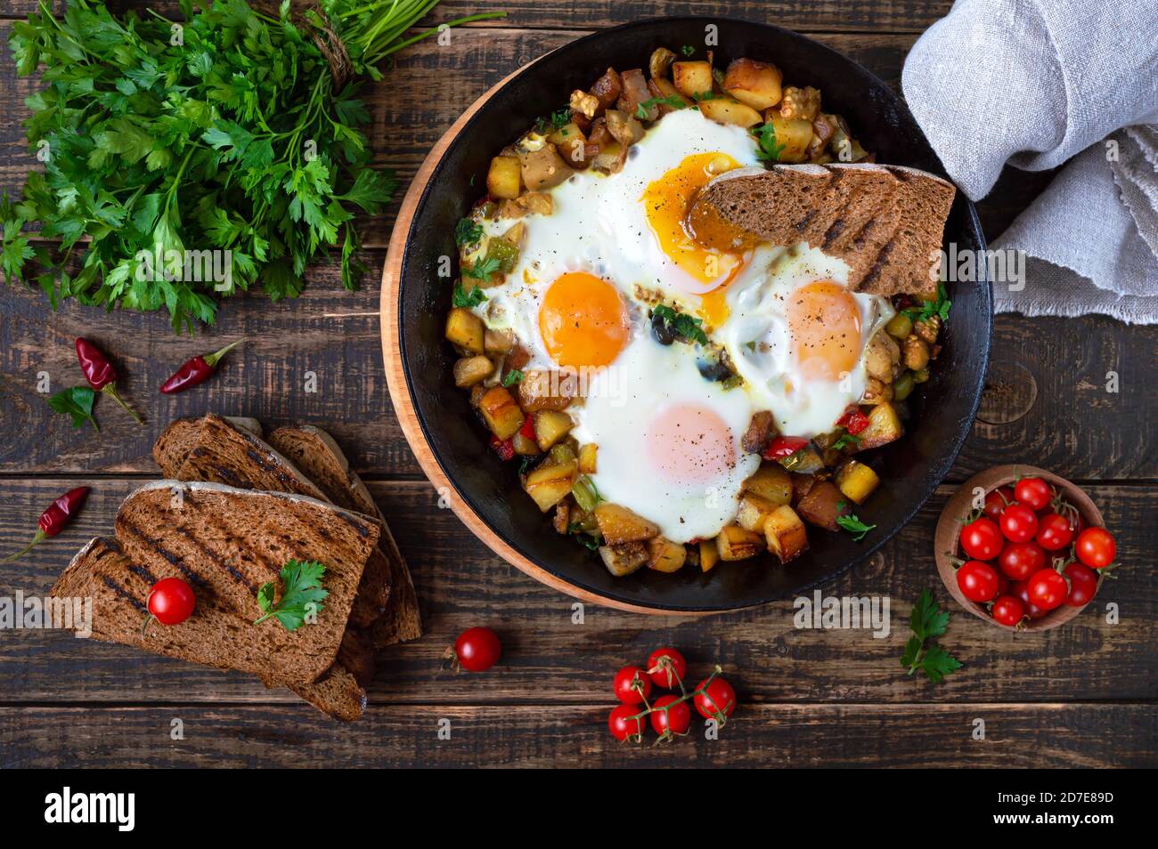 Spiegeleier mit Gemüse - shakshuka in der Pfanne und Roggenbrot auf einem alten hölzernen Hintergrund. Spätes Frühstück. Rustikaler Stil. Mittelöstlicher Tradit Stockfoto