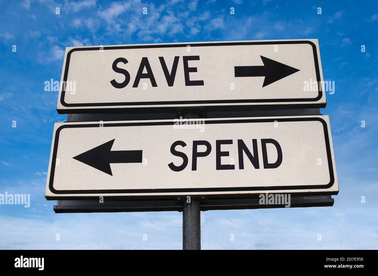 Sparen im Vergleich zu Ausgaben. Weiße zwei Straßenschilder mit Pfeil auf Metallmast mit Wort. Richtungsstraße. Kreuzung Straßenschild, Zwei Pfeil. Blauer Himmel Hintergrund. Stockfoto