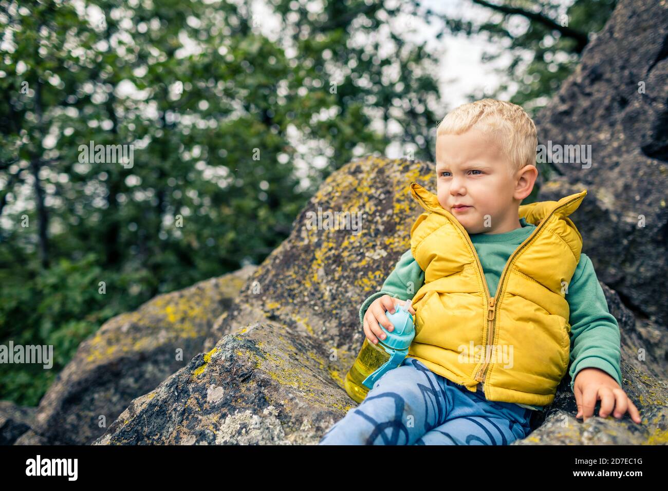 Kleiner Junge wandern in den Bergen, Familienabenteuer. Kleines Kind, das im felsigen grünen Wald spazierengeht, lächelnd. Stockfoto