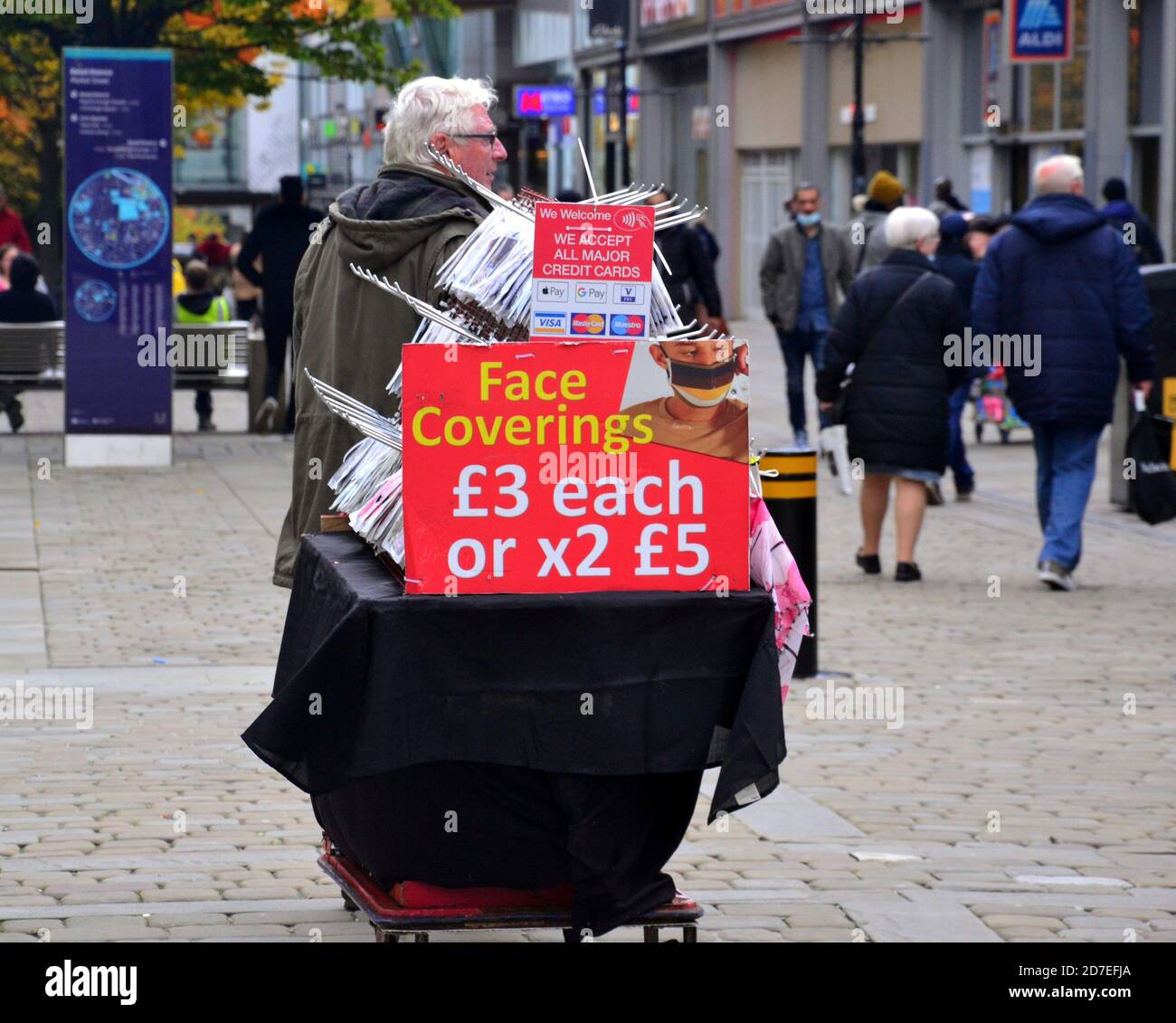 Covid 19 oder coronavirus Beschilderung und Werbung in Manchester, Greater Manchester, England, Vereinigtes Königreich. Ein Mann verkauft Gesichtsbezüge und Masken auf der Market Street im Zentrum von Manchester. Stockfoto