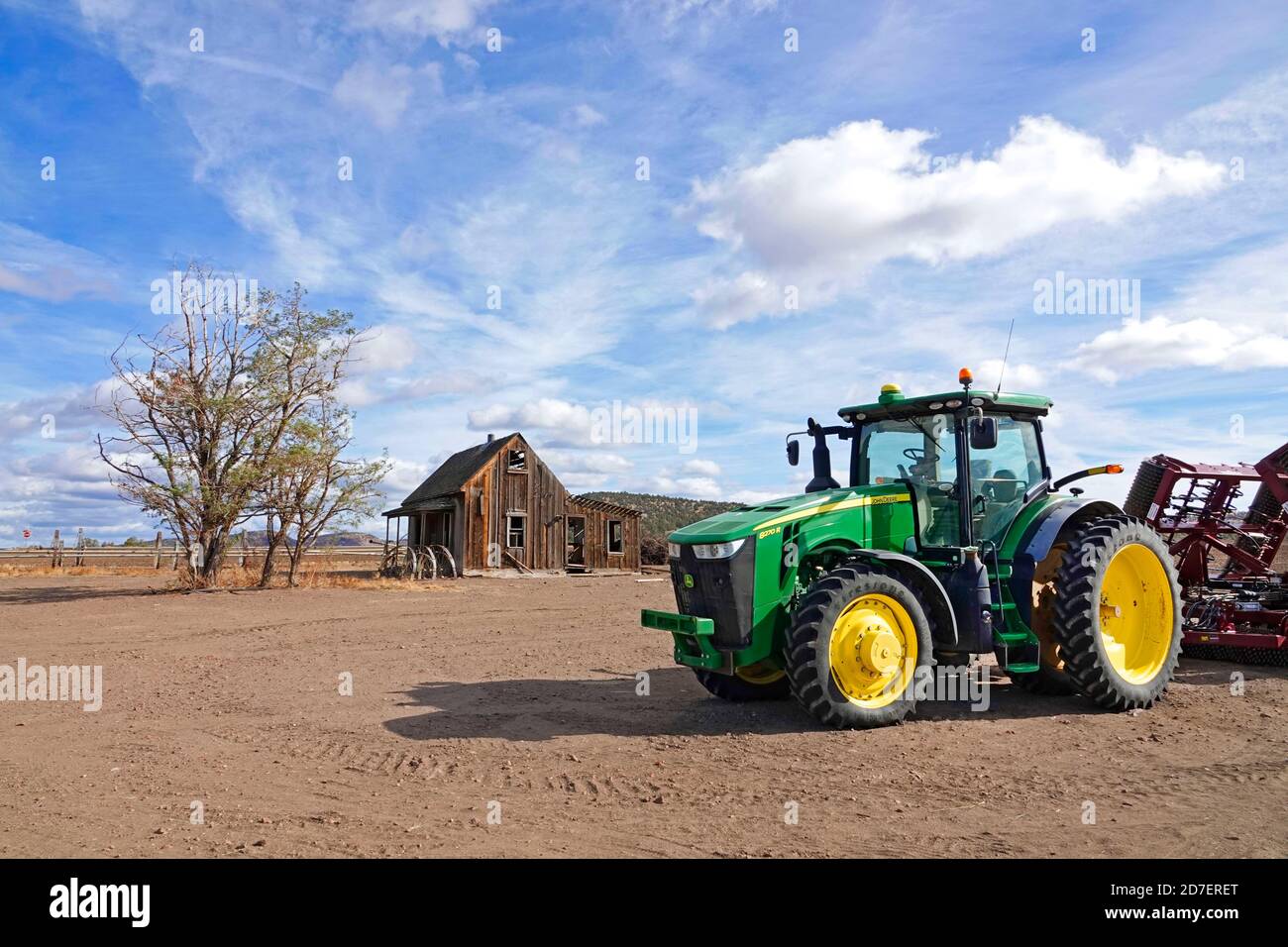 Ein neuer Traktor von John Deere, der einen Scheibenpflug zieht, befindet sich in der Nähe eines verlassenen Bauernhauses aus der Zeit der Depression in der Nähe der kleinen Bauernstadt Culver im Zentrum von Oregon. Stockfoto