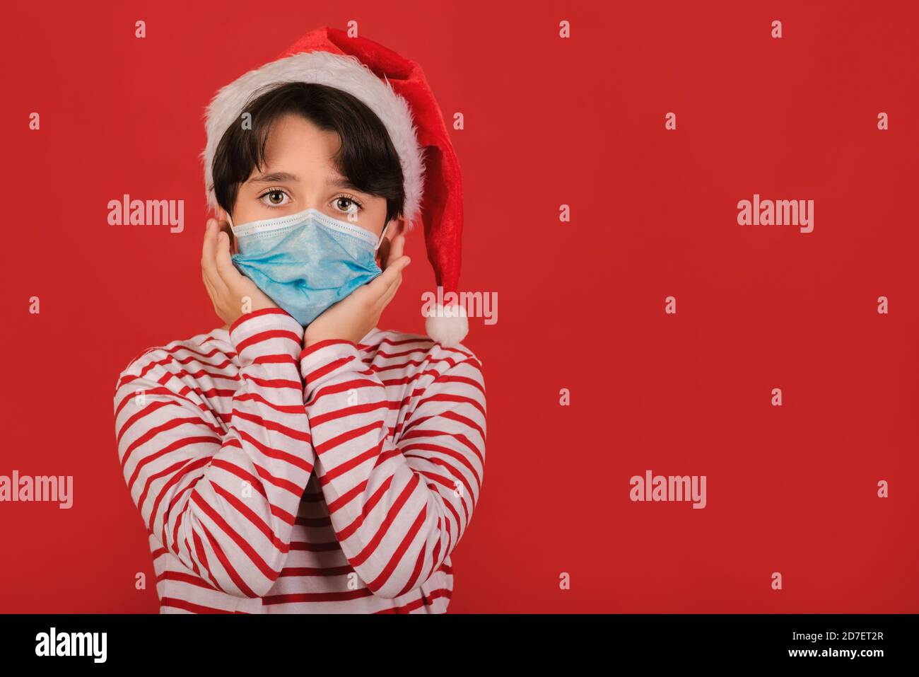 Frohe Weihnachten, lustiges Kind mit medizinischer Maske trägt Weihnachtsmann Hut Auf rotem Hintergrund Stockfoto