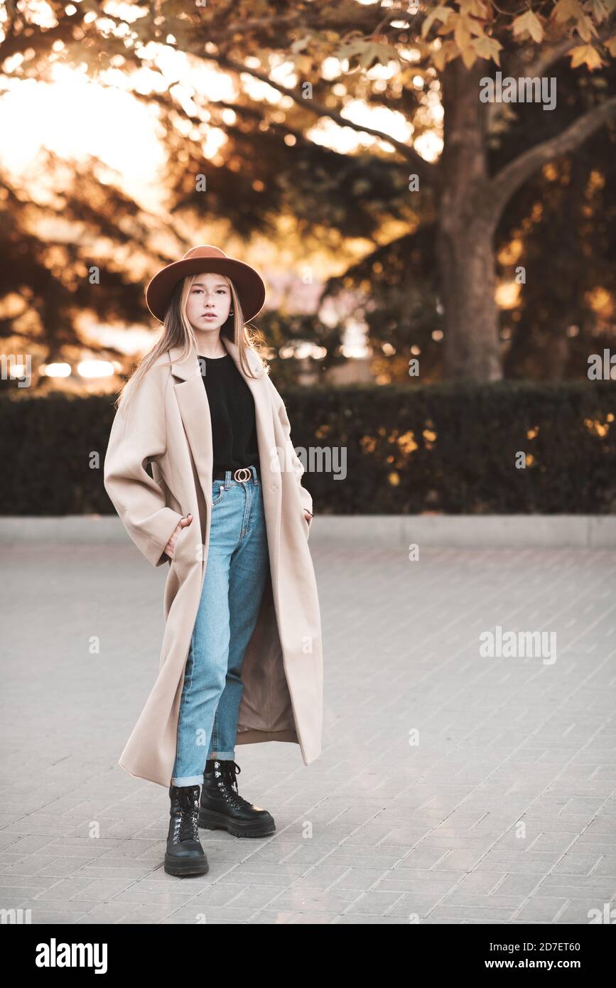 Blonde Teenager-Mädchen 13-14 Jahre alt trägt stilvolle Mantel und Hut zu  Fuß in der Stadt Straße mit Händen in den Taschen über Herbst Natur  Hintergrund Nahaufnahme. Fallen Stockfotografie - Alamy