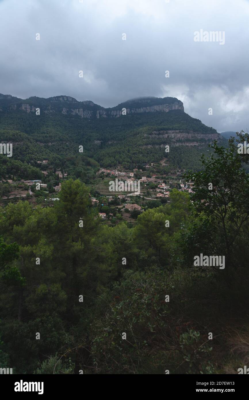 Blick auf die kleine Stadt Gallifa und ihre Berge in Katalonien, Spanien bei einem Sturm im Morgengrauen. Vertikal. Kleine Häuser mit Lichtern Stockfoto