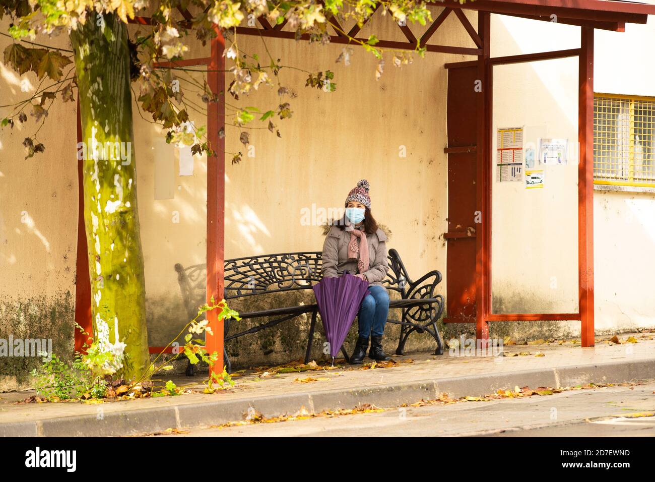 Frau mit Sonnenschirm sitzt an der Bushaltestelle Stockfoto