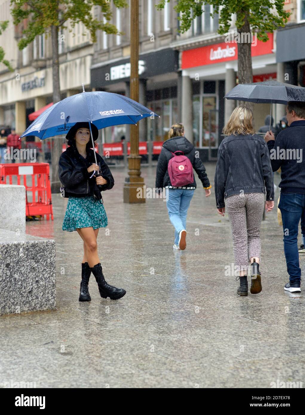 Junge Frau, die Demonstration im Regen mit Regenschirm beobachten. Stockfoto