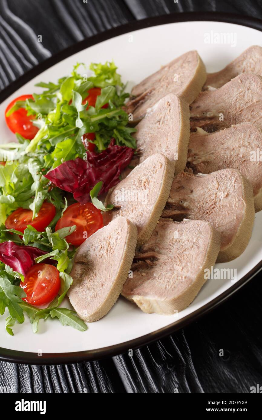 Aufschnitt von Rindfleisch Zunge serviert mit frischem Salat Nahaufnahme auf dem Teller auf dem Tisch. Vertikal Stockfoto