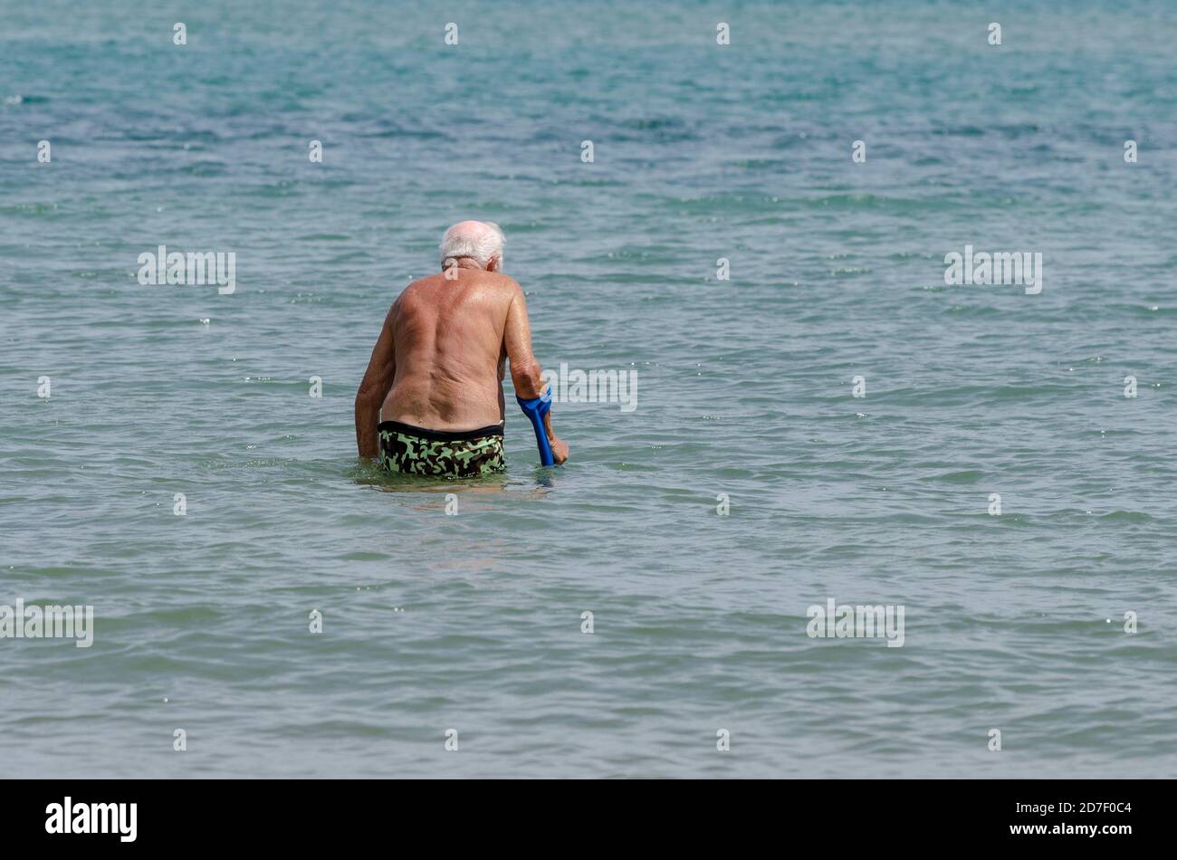 Der alte Herr am Meer läuft und tritt ins Wasser ein Mit dem Stick Stockfoto