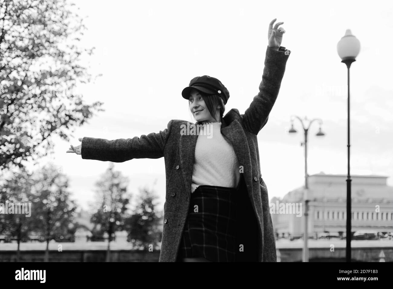 Glücklich stilvolle Frau wirbeln auf einer Straße mit ausgebreiteten Händen. Schwarz-weiß getönte dynamische Porträt in Parisien-Stil Stockfoto