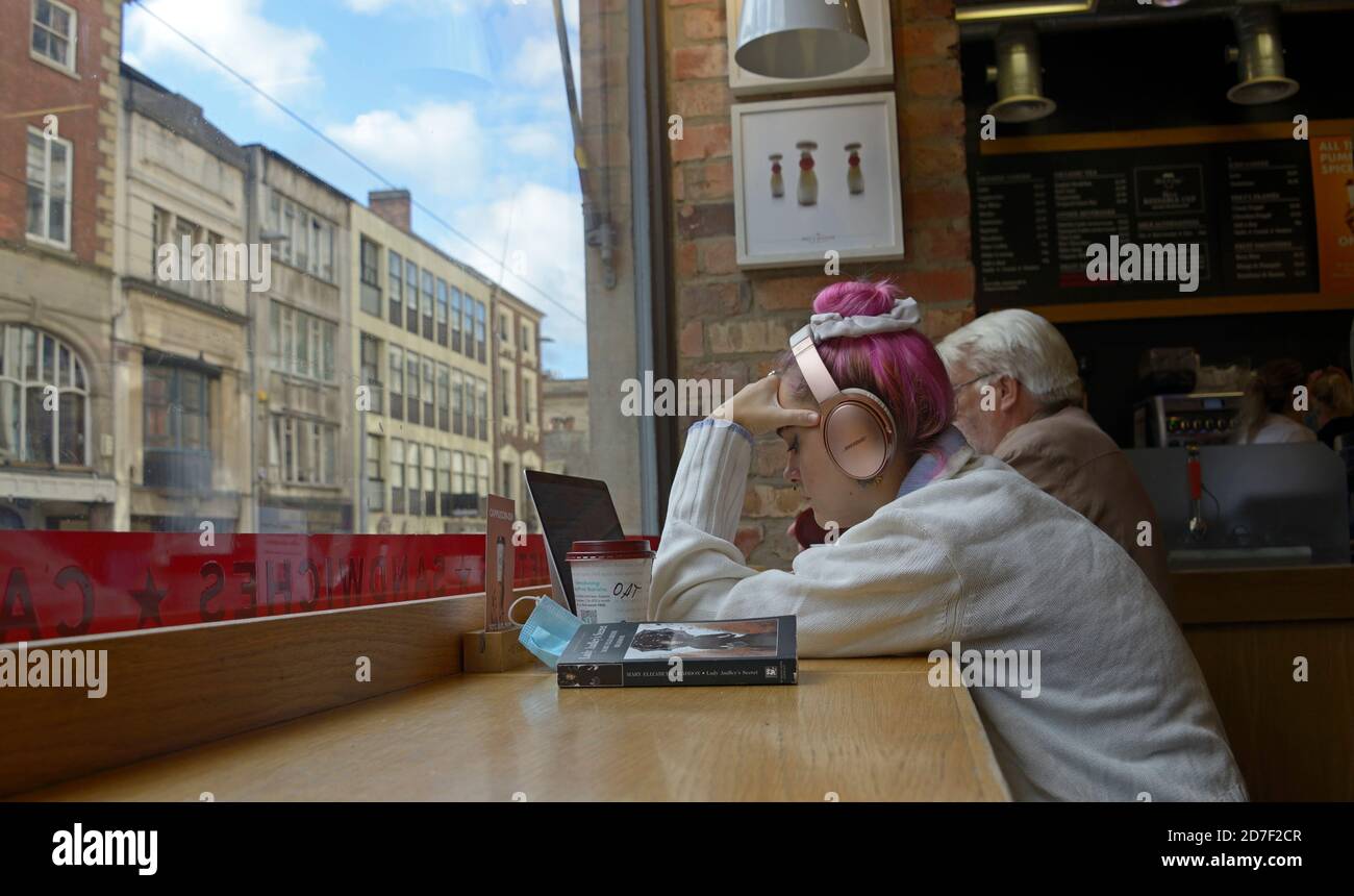 Student mit rosa Haaren, am Computer im Cafe', mit Kopfhörern an. Stockfoto