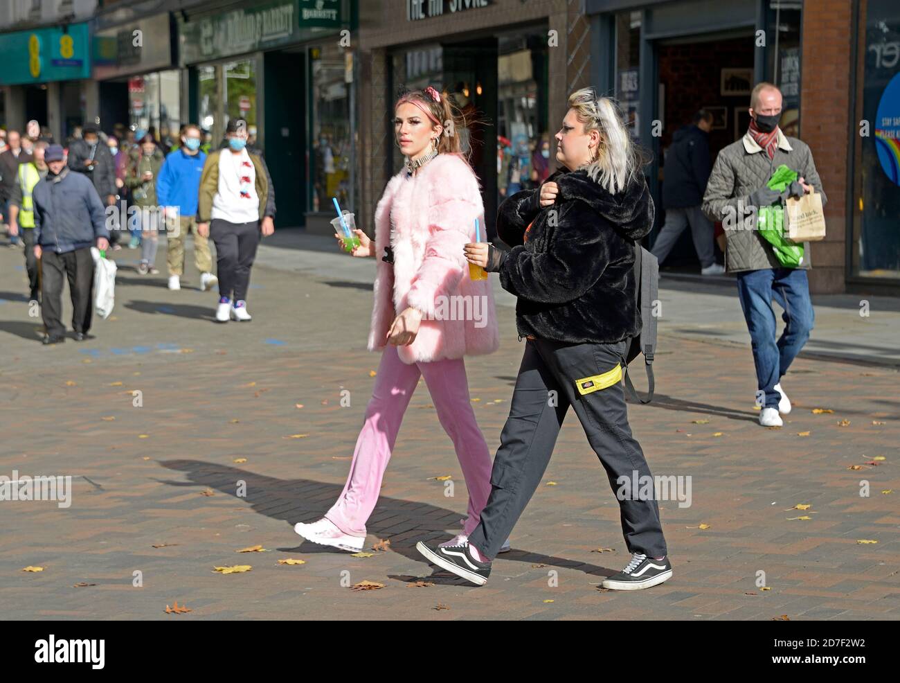 Junge Frauen in Kunstpelzjacken, die durch das Stadtzentrum hindurchstochen. Eine in Rosa, eine in Schwarz. Stockfoto