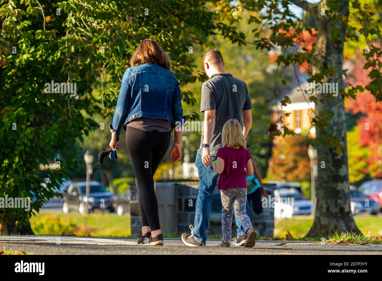 Eine junge kaukasische Familie von drei Kindern geht an einem schönen Herbstnachmittag im Park spazieren. Das süße kleine blonde Mädchen folgt ihrem Papa und ihrer Mama. Sie A Stockfoto