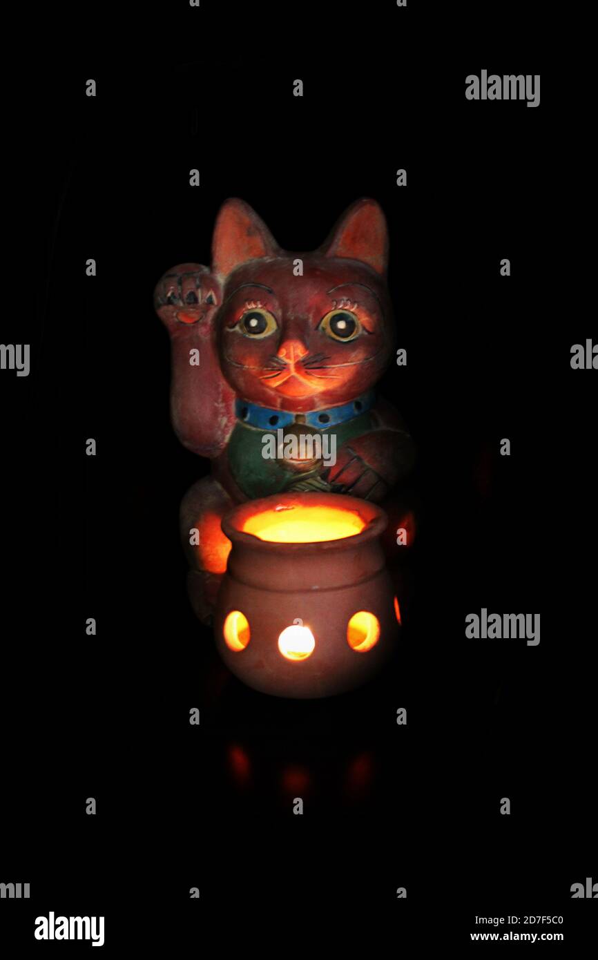 Meine japanische winkende Katze, genannt Maneki Neko, bei Kerzenlicht Stockfoto