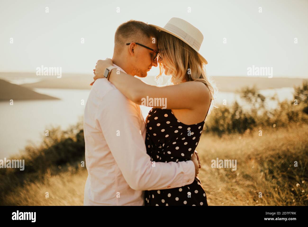 Ein Mann mit einer Frau in einem Hut Umarmung und Kuss in das hohe Gras auf der Wiese Stockfoto