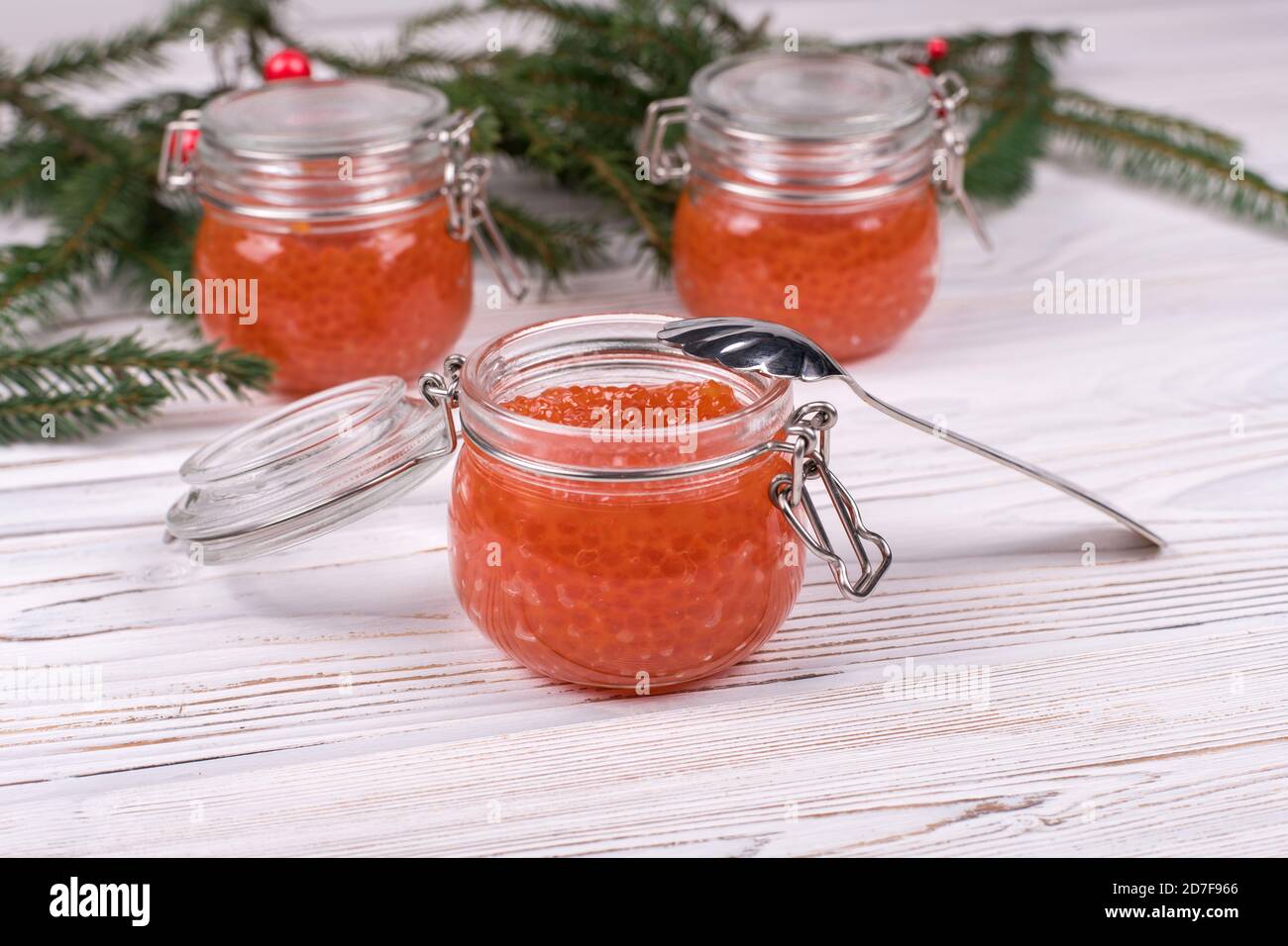 Roter Kaviar in einem Glas auf einem würzigen weißen Holzhintergrund mit einem Weihnachtsbaum. Das Hauptgericht des neuen Jahres. Stockfoto