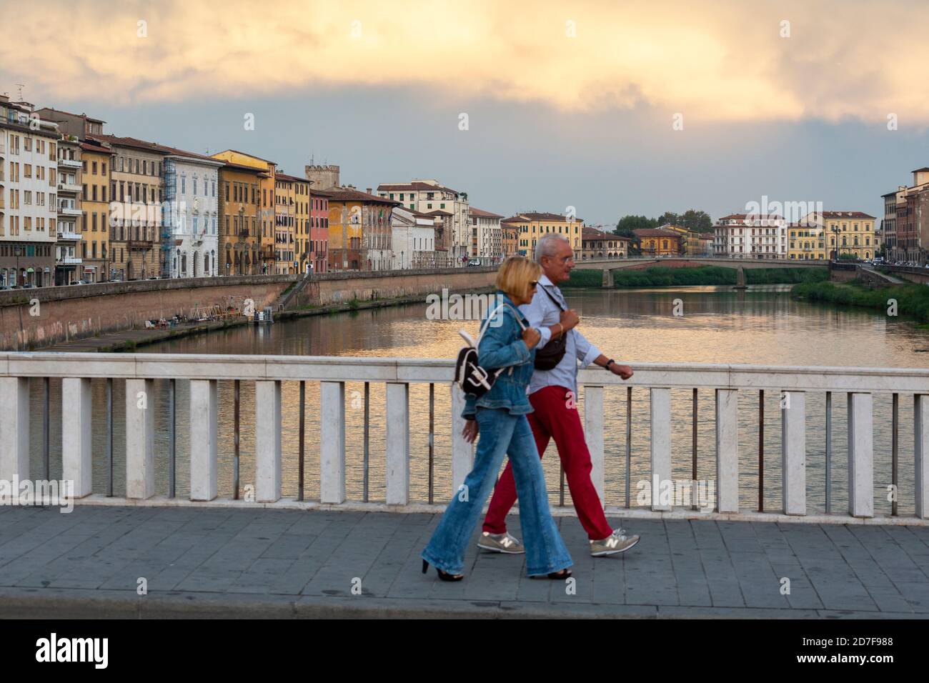 Ein älteres Paar, das bei Sonnenuntergang die Ponte Di Mezzo Brücke über den Fluss Arno überquert, Pisa, Toskana, Italien Stockfoto