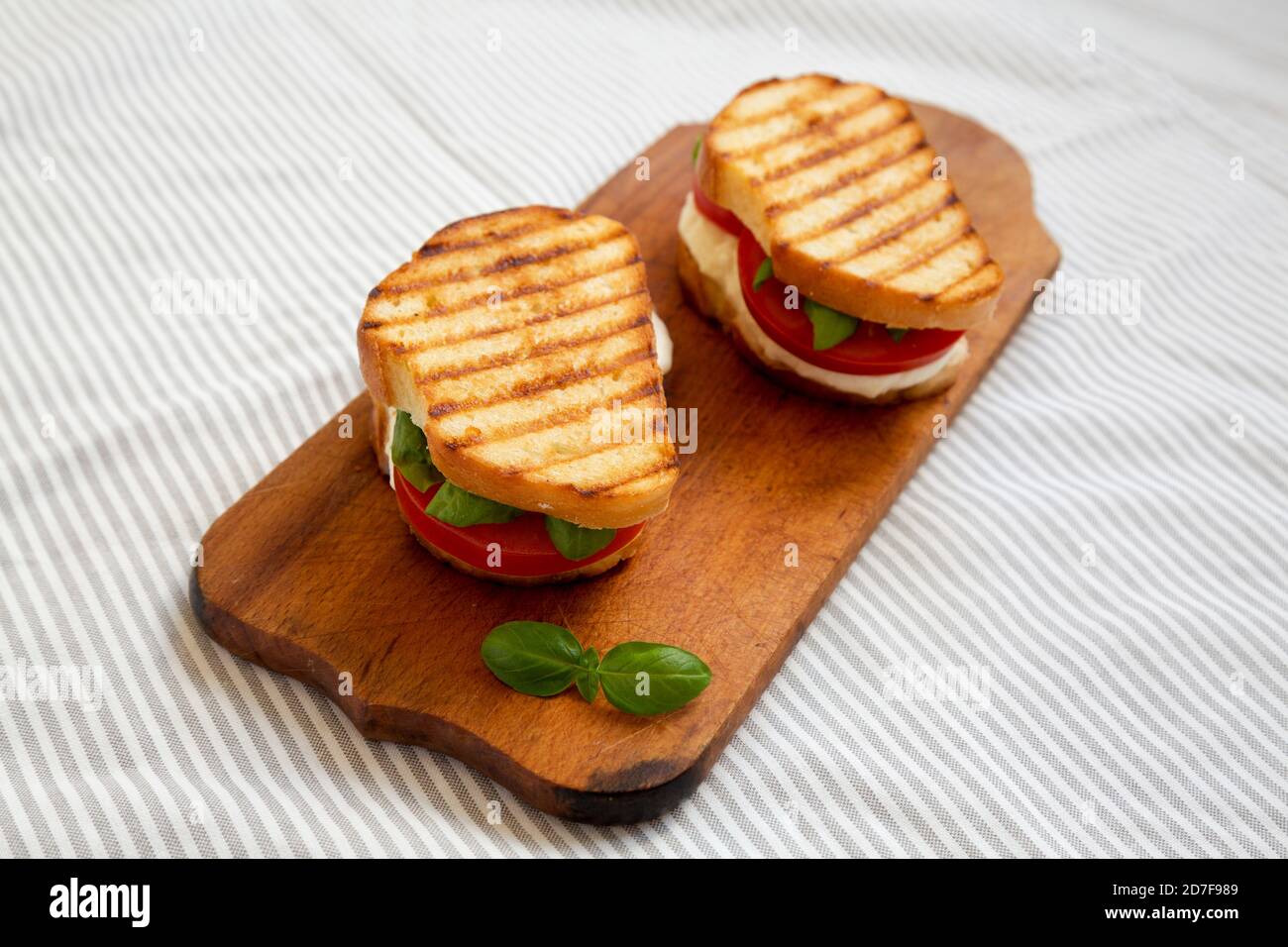 Leckere gegrillte Caprese Panini (Mozzarella, Tomaten und Basilikum) auf einem rustikalen Holzbrett, Seitenansicht. Stockfoto