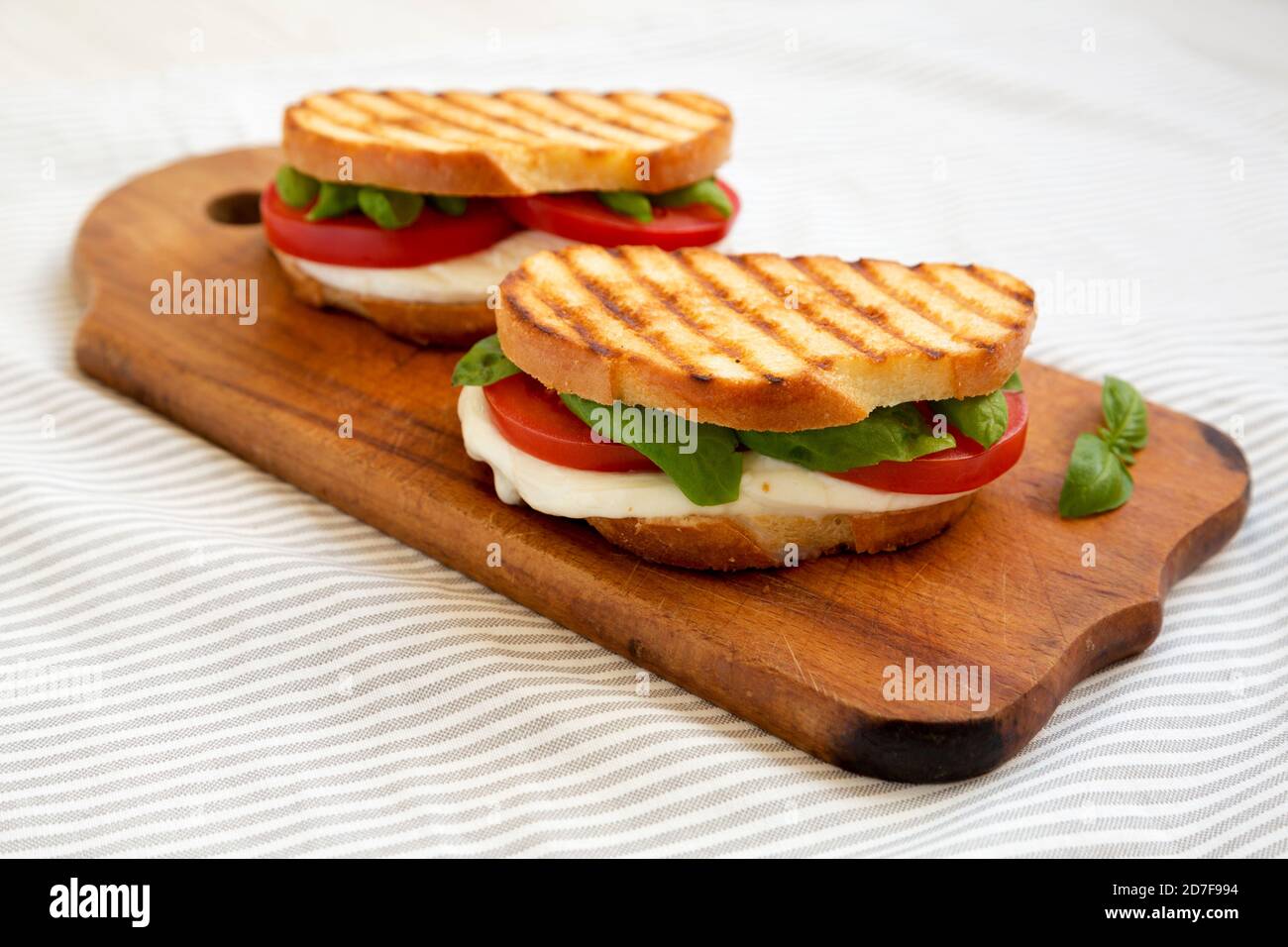 Leckere gegrillte Caprese Panini (Mozzarella, Tomaten und Basilikum) auf einem rustikalen Holzbrett, Seitenansicht. Stockfoto