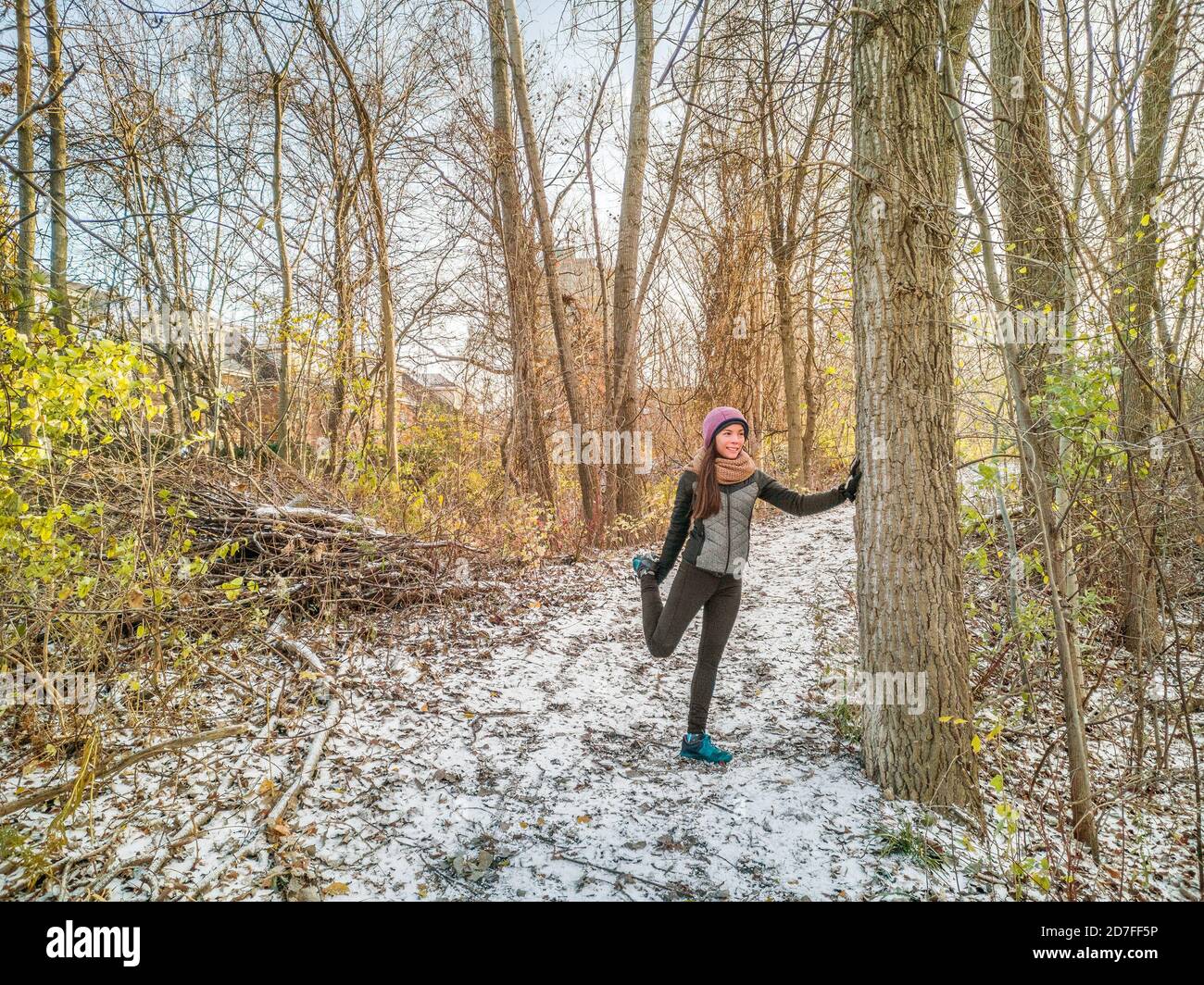 Winter Running Athlet Frau auf kalten Trail laufen immer bereit Stretching Beine für Joggen außerhalb Wald Training tragen warme Kleidung Handschuhe, Winter Stockfoto