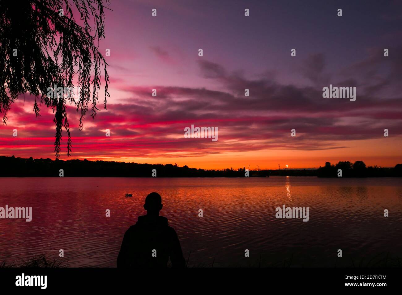 Silhouette eines Mannes vor dem Wasser mit herrlichem Sonnenuntergang. Schöne Landschaft mit einem See und dramatischen Himmel mit Cumulus Wolken am Horizont. Wir Stockfoto