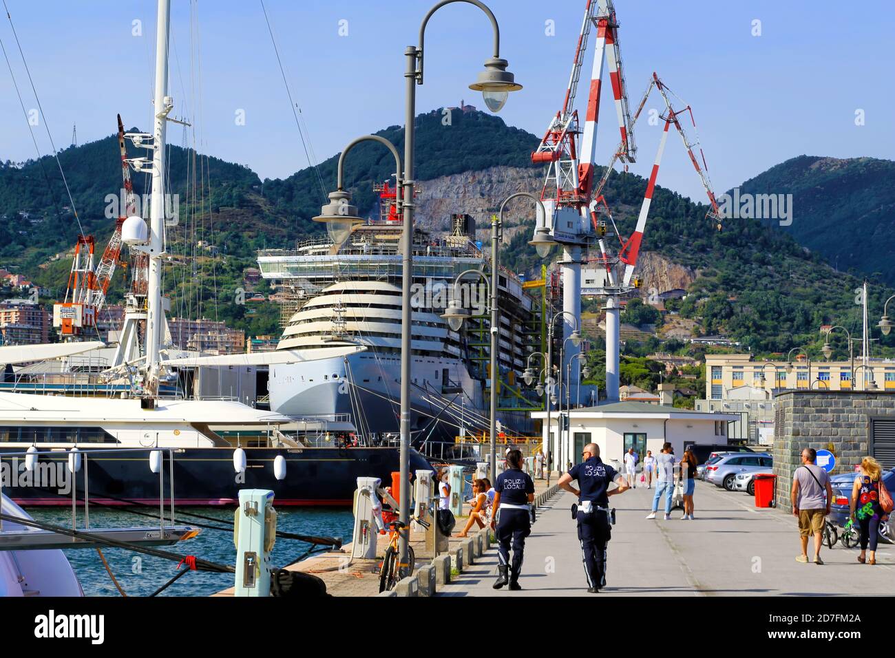 Menschen zu Fuß und entspannen in der Marina von Marina Genova Flughafen. Im Hintergrund die historischen Werften von Sestri Ponente mit einem Kreuzfahrtschiff unter Stockfoto