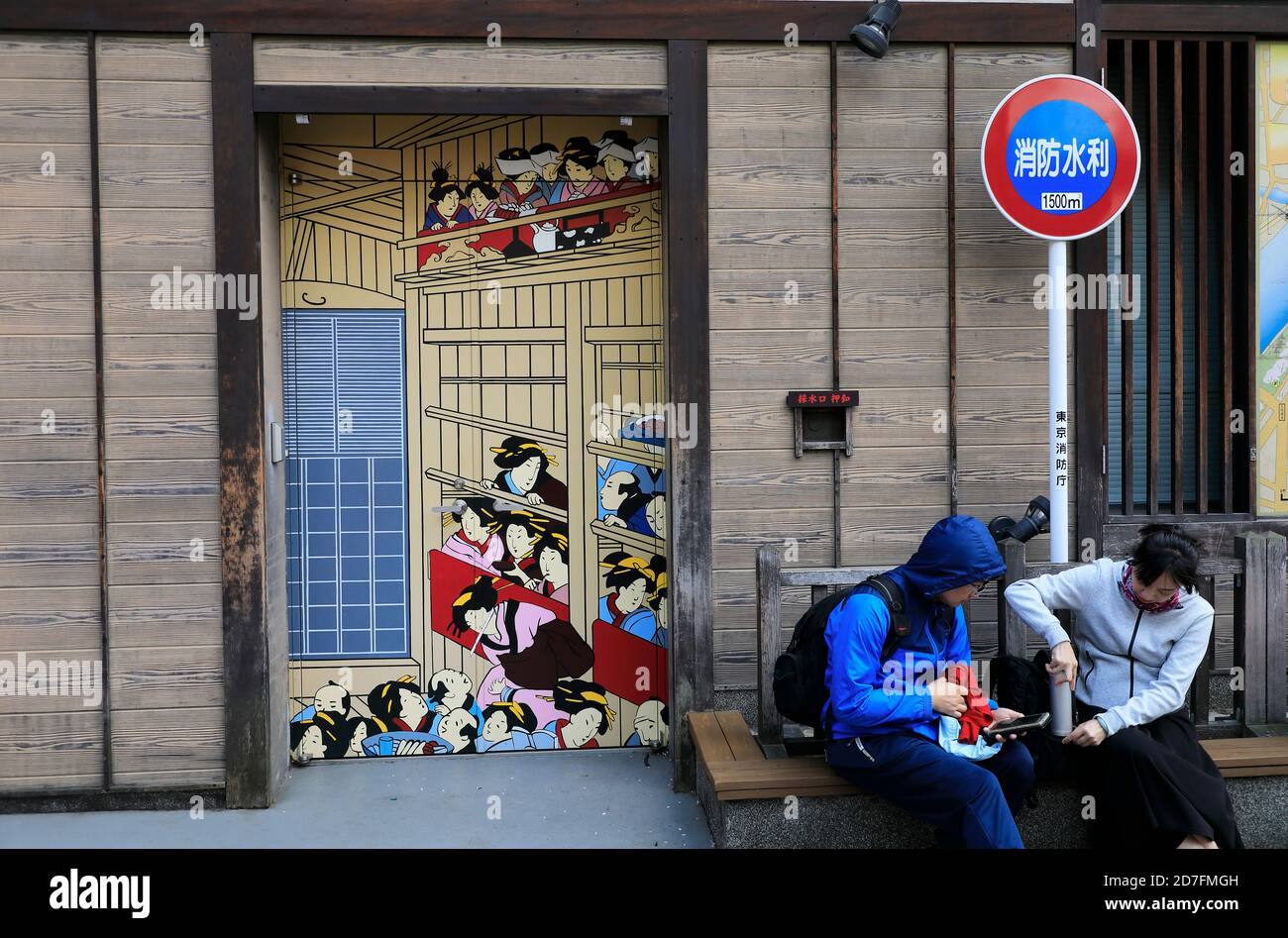 Touristen ruhen auf Bürgersteig mit einem traditionellen Ukiyoe Gemälde dekoriert Tür und ein Löschhydrant waring Zeichen hinter.Asakusa.Tokyo.Japan Stockfoto