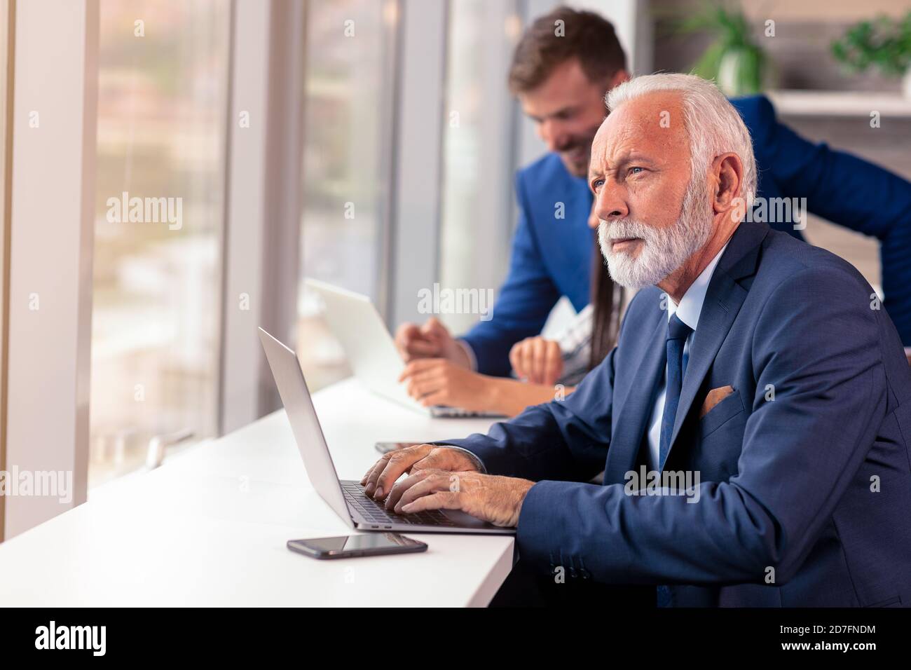 Senior Manager mit einem Laptop mit jungen Kollegen im Hintergrund Stockfoto
