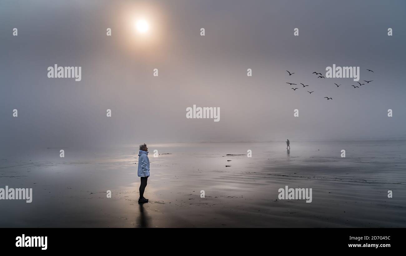 Ältere Frau, die in den dichten Nebel über dem Pazifischen Ozean in Cox Bay im Pacific Rim National Park auf Vancouver Island, British Columbia, blickt, Stockfoto