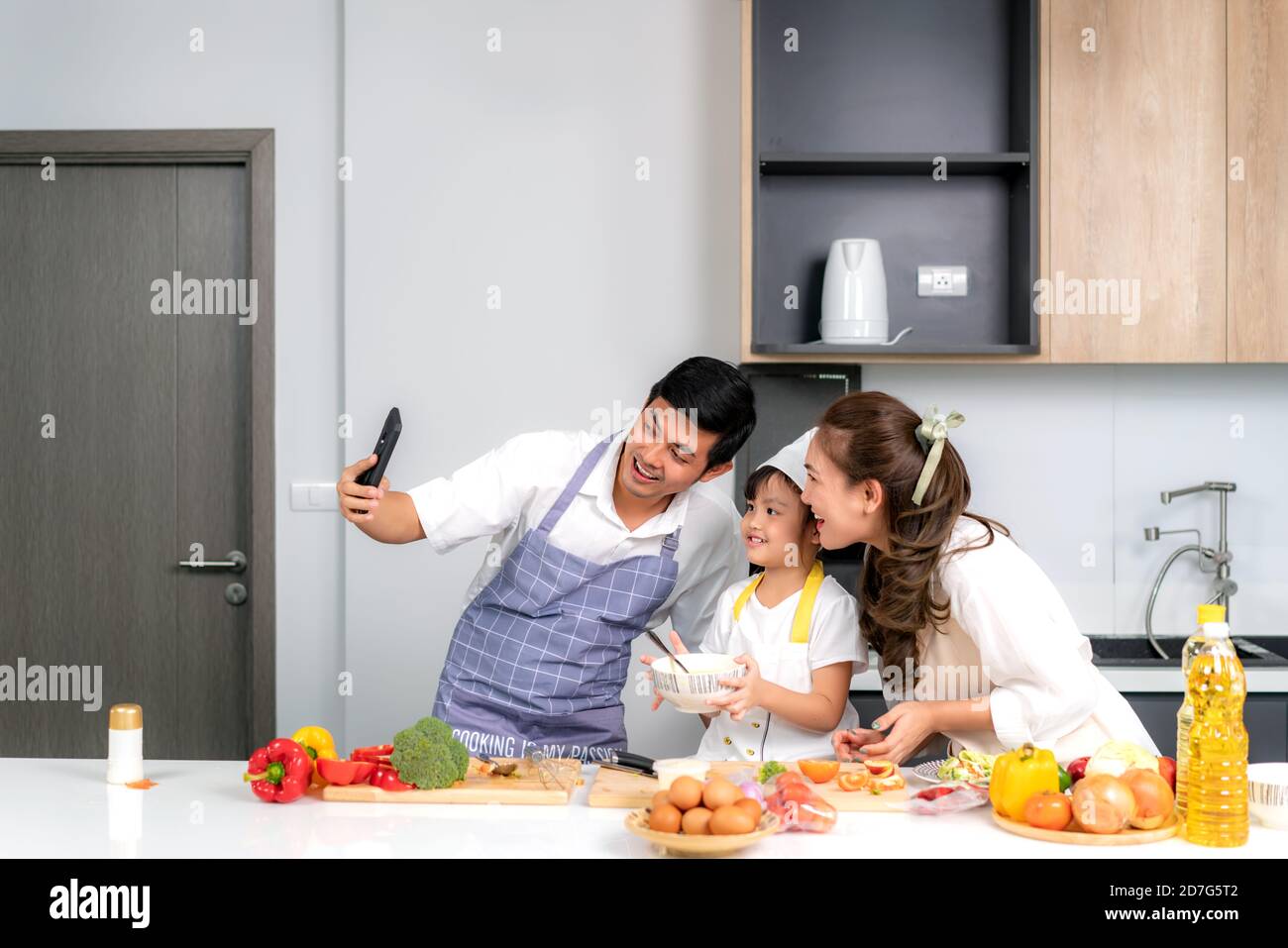 Junge asiatische Familie bereiten Salat in der Küche und Vater nehmen ein Foto Selfie per Telefon. Aufgeregt lächeln und Fällen glücklich. Eltern lehren Tochter Stockfoto