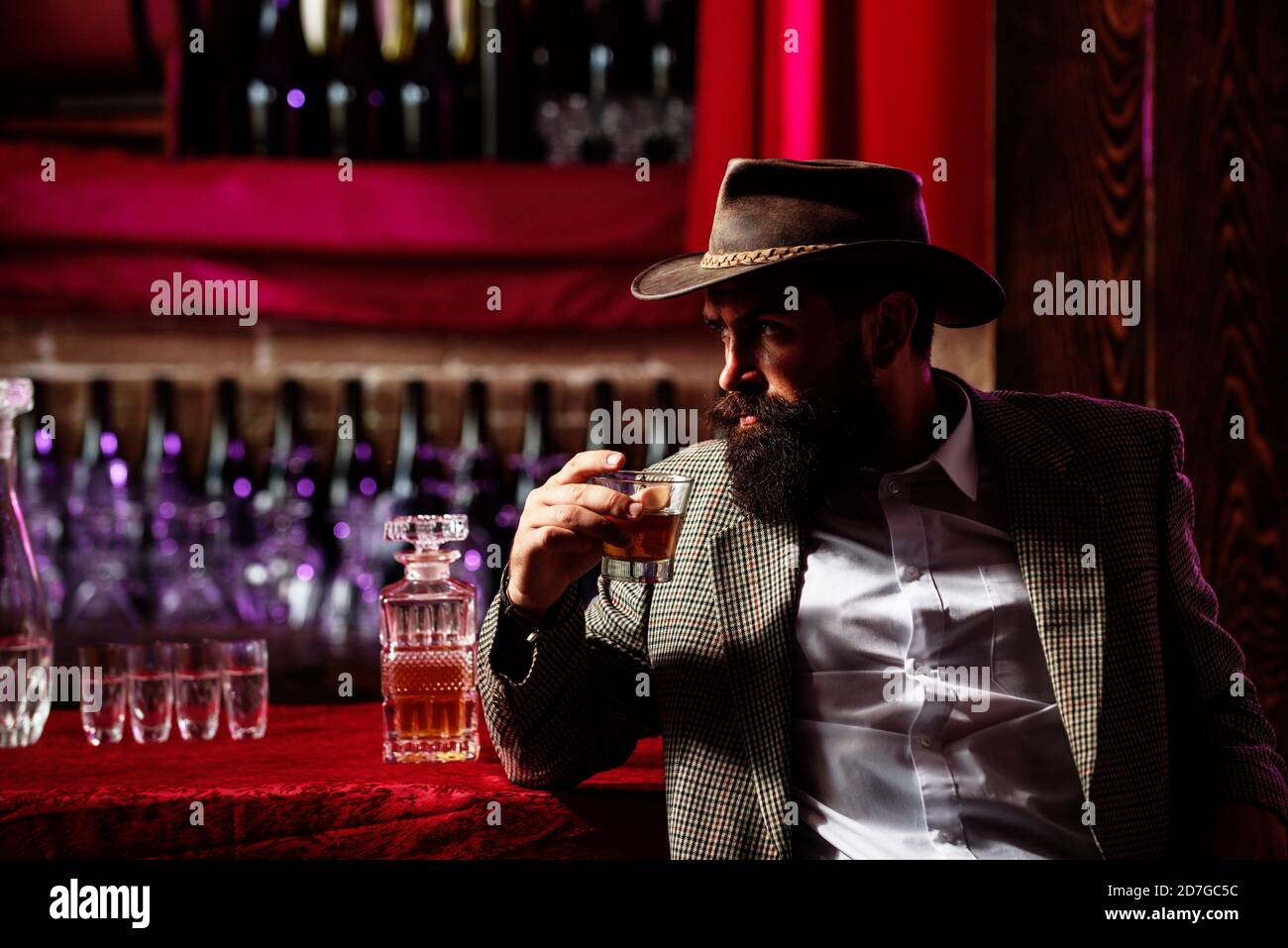 Mann mit Bart hält ein Glas Brandy. Verkostung und Degustation. Bärtiger Kerl im Retro-Anzug mit Glas Whiskey. Teure Getränke. Vintage Barkeeper mit Stockfoto