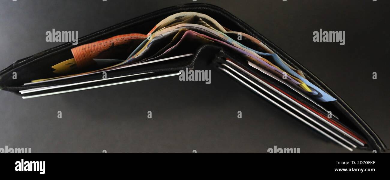 Eine interessante Luftaufnahme von oben Grundriss einer schwarzen Brieftasche gefüllt mit Bargeld-Dollar-Noten. Kreditkarten sichtbar und verschiedene farbige Währung Stockfoto