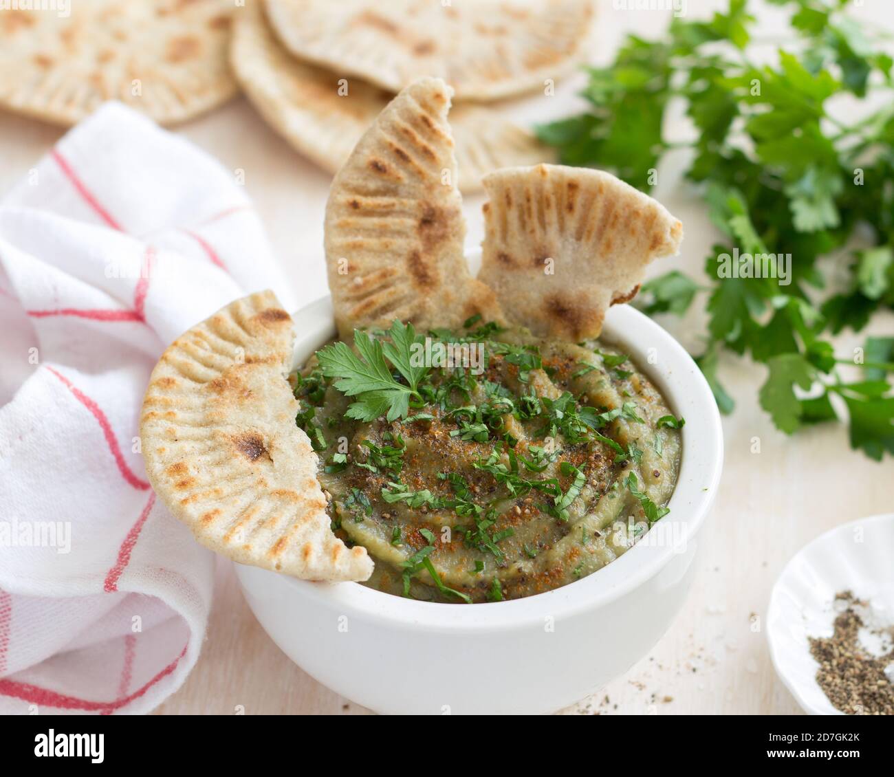 Auberginen tauchen Sie in eine weiße Keramikschale mit Petersilie und Vollkornbrot auf hellem Holzhintergrund Stockfoto