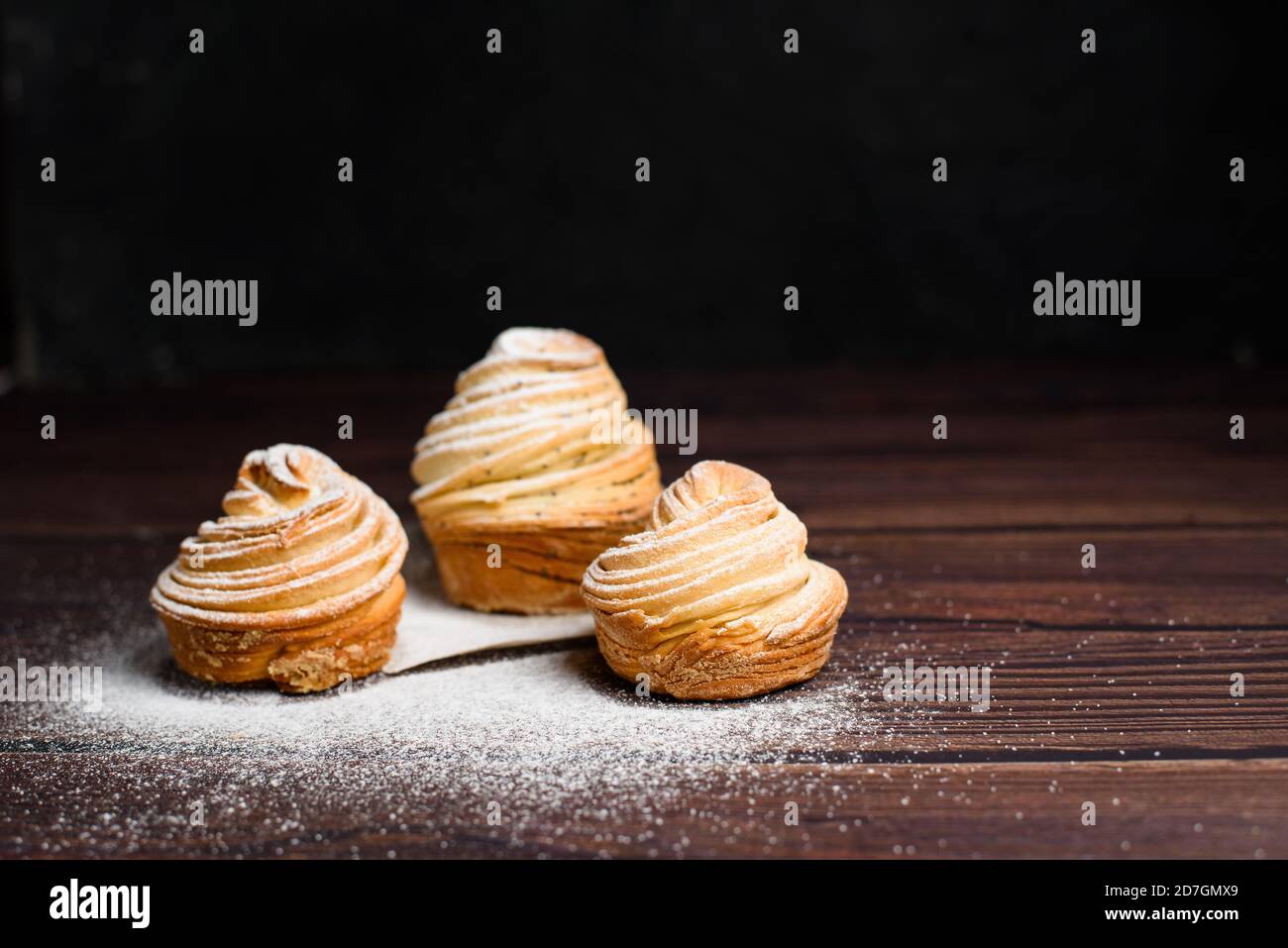 Moderne Cruffins werden aus Blättercroissants in Form eines Muffins hergestellt. Auf dunklem Grund in Puderzucker. Platz kopieren. Die Ansicht von oben. clos Stockfoto