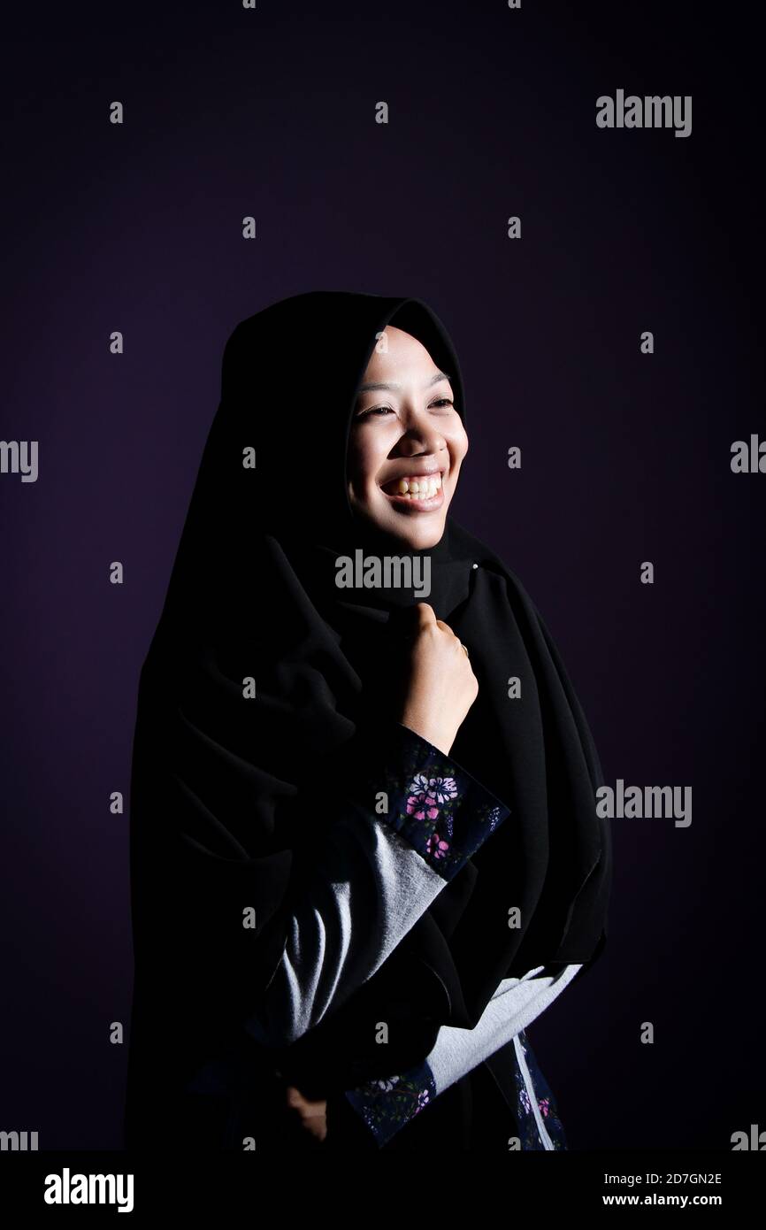 Porträt einer asiatischen Frau in einem Hijab in dunklem Licht. Der glückliche Ausdruck einer muslimischen Frau mit einem schwarzen Schleier Stockfoto