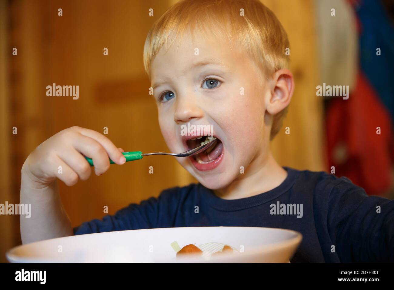 Kleiner Junge mit offenem Mund, der alleine am Tisch isst. Stockfoto