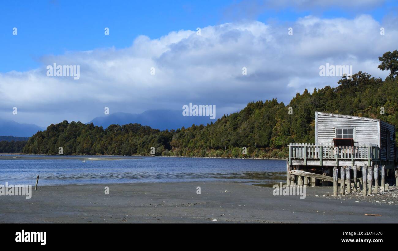 Okarito Lagune an der Westküste der Südinsel Neuseelands. Im Vordergrund ist der alte Bootsschuppen mit den südlichen Alpen dahinter Stockfoto