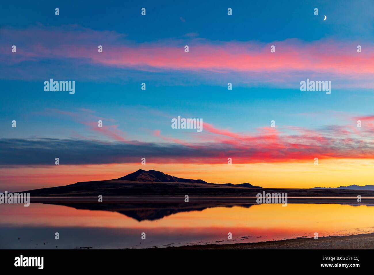 Das Bild von Antelope Island spiegelt sich auf dem Wasser des Großen Salzsees, während der Sonnenuntergang Nachglühen in den Wolken darüber reflektiert. Stockfoto