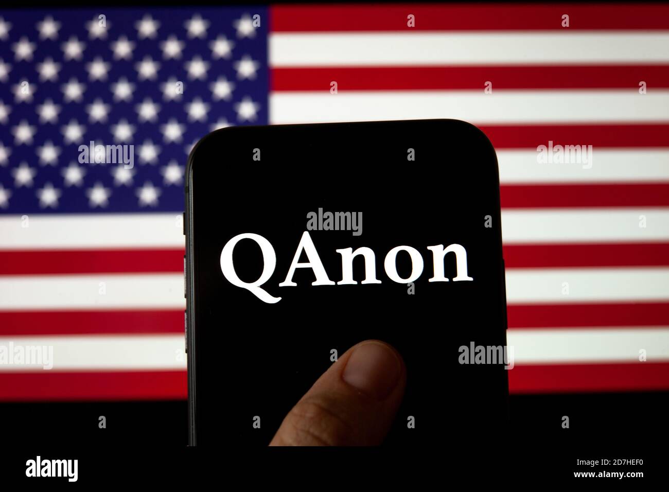 QAnon-Logo auf dem Smartphone, das auf der USA-Flagge platziert ist. Konzept für QAnon oder Q Anon, eine Verschwörungstheorie des tiefen Staates. Stockfoto