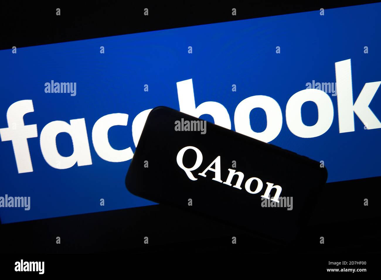 QAnon im Vergleich ZU FACEBOOK. QAnon-Unternehmenslogo auf dem Smartphone, das auf Facebook-Logos platziert ist. Konzept für das Verbot von QAnon in sozialen Medien. Stockfoto