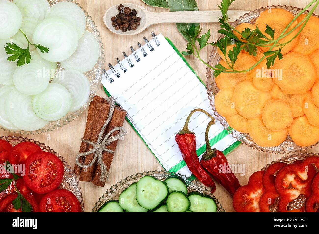 Frisches, gehacktes Gemüse, Gewürze und ein Notizbuch mit Rezepten auf einem Holzschneidetisch. Stockfoto