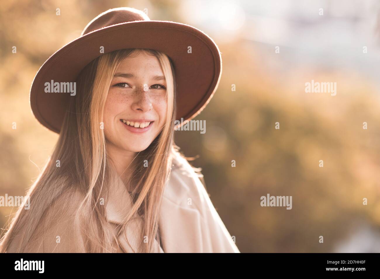 Lächelndes Teenager-Mädchen 13-14 Jahre alt trägt Hut und Mantel über Herbst Natur Hintergrund Nahaufnahme. Blick auf die Kamera. Teenagerhood. Glück. Stockfoto