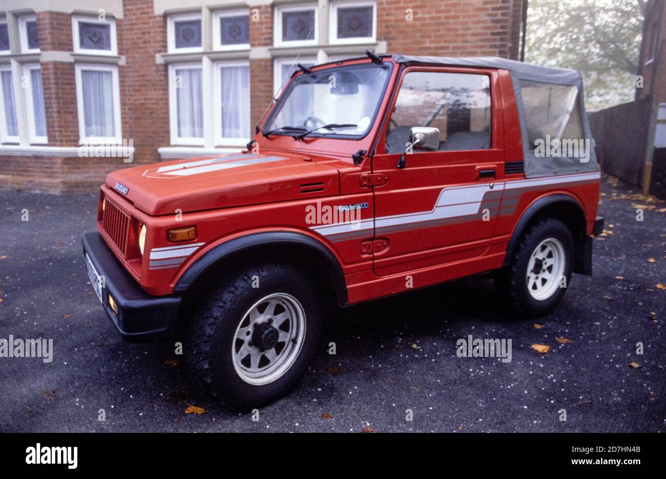 Ein roter Suzuki SJ410 Jeep vom Typ 1987 mit grauen Streifen und einem grauen Vinyl-Softtop, der auf dem Vorplatz eines Wohnblocks im Boscombe-Gebiet von Bournemouth abgestellt ist. 06. Oktober 1990. Foto: Neil Turner Stockfoto