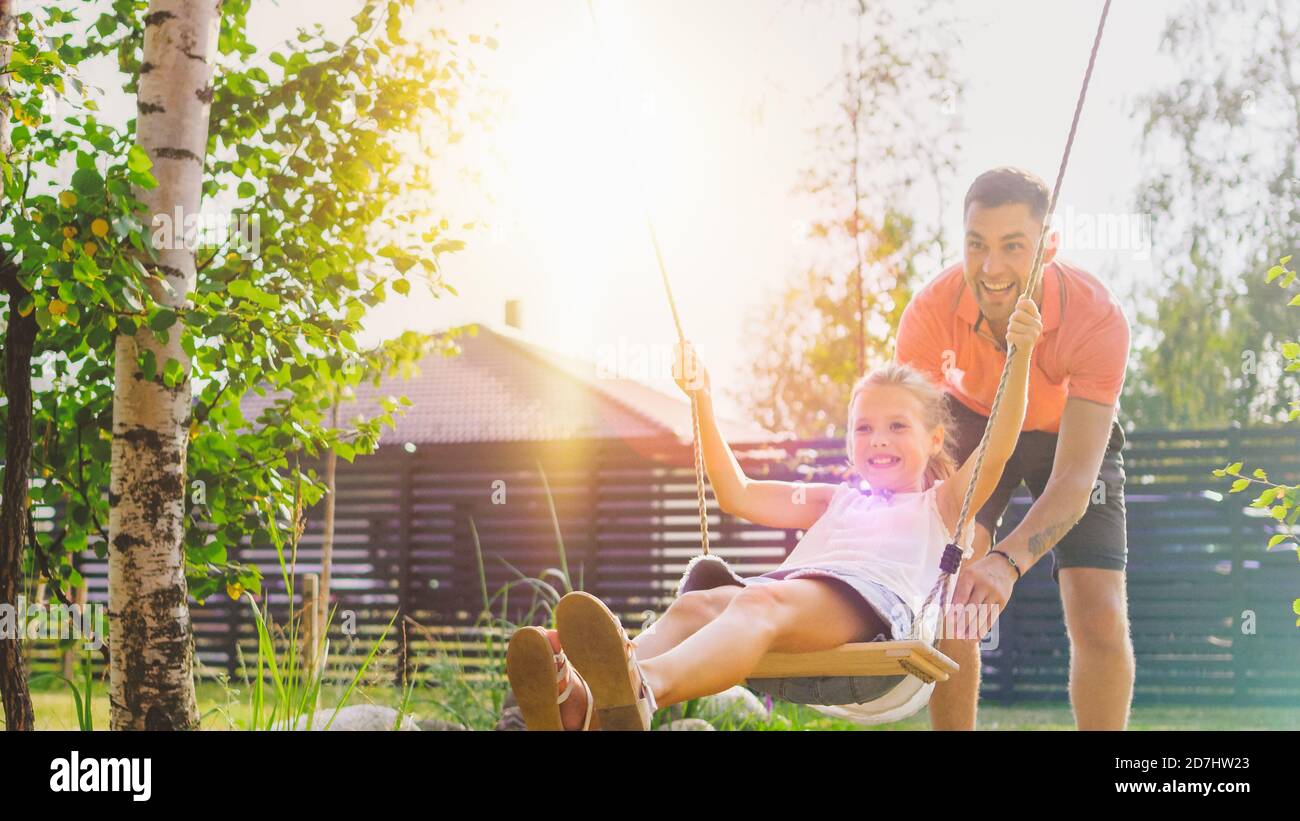 Freudig Vater schiebt Schaukeln mit seine nette kleine Tochter auf sie. Happy Family verbringt Zeit zusammen an einem sonnigen Sommertag im Garten von Idyllics. Stockfoto