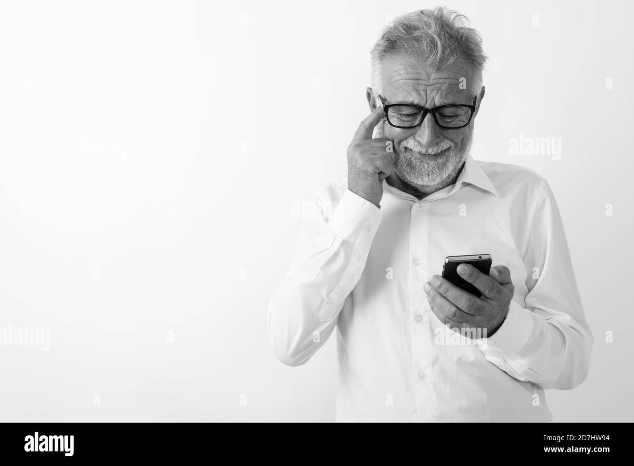Studio geschossen von traurigen älteren bärtigen mit Handy während Kratzen Kopf mit Brille vor weißem Hintergrund Mann Stockfoto