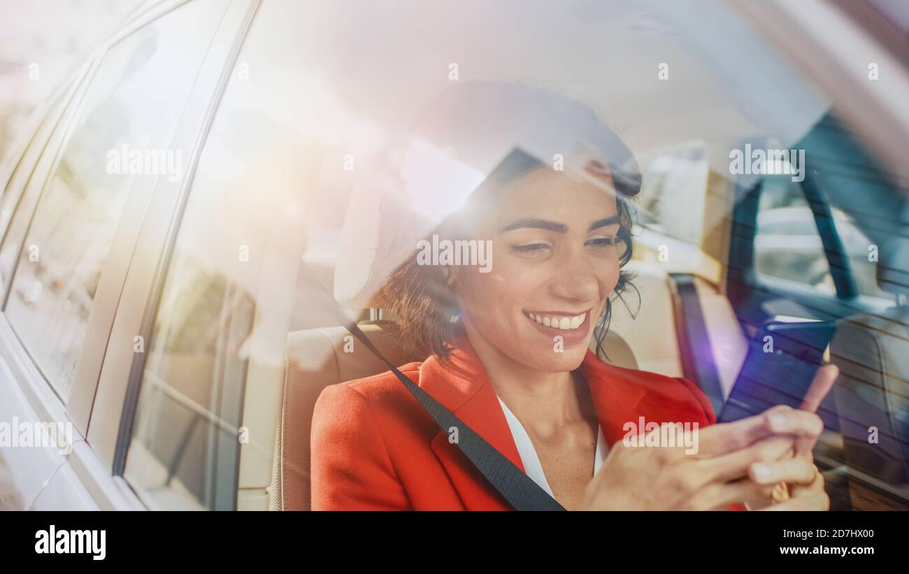 Schöne Frau Reisen in einem Auto, sitzen auf einem Beifahrersitz verwendet Smartphone, Typen Nachricht, browses through Internet. Kamera Aufnahme von außerhalb des Stockfoto